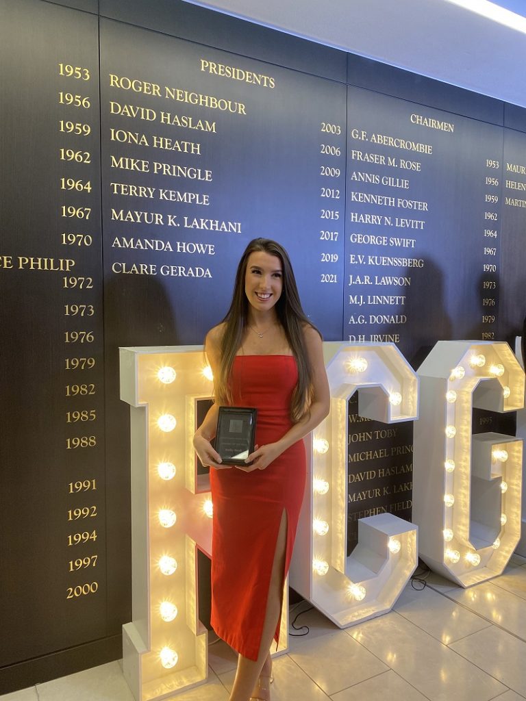 Holly holds her award infront of illuminated background